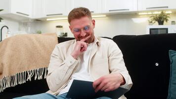 jong Mens Bij huis tocht dagelijks plan in notitieboekje sets prioriteiten en schrijft gemakkelijk schema voor taken. Kaukasisch vent Aan sofa lijsten doelen voegt toe tijd blokken en houdt focus met kalmte humeur en Doorzichtig verstand. video