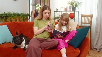 mor och dotter med franska bulldogg på Hem använda sig av smartphone för matematik handledning mor förklara exempel dotter notera. kvinna och flicka med hund på soffa lösa uppgift visa hurra leende lära sig med glädje Mer video