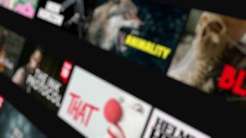 Blurry mock-up of a dark-themed streaming platform, featuring rows of rectangular tiles with fictional movie and TV show thumbnails video