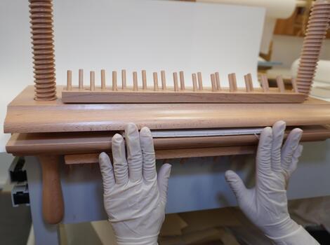 Gloved hands install a block of sheets in a wooden bookbinding press. Spine alignment, manual restoration, workshop. photo