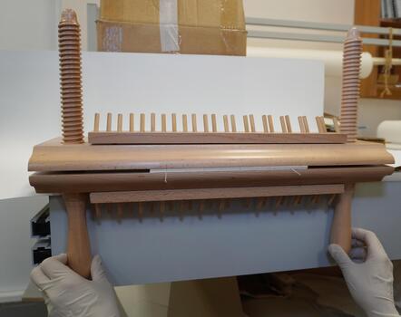 Gloved hands hold a wooden bookbinding press with a rack and screw posts. Setting up the equipment in the workshop, horizontal frame. photo