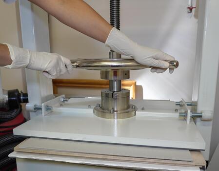 Gloved hands rotate the handle of the screw press. Paper pressing and straightening, bookbinding workshop, close-up. photo