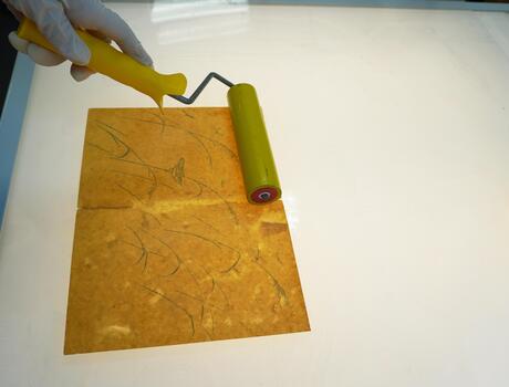 A gloved hand rolls a drawing on a light table with a rubber roller. Orange paper, sheet alignment, archival restoration. photo