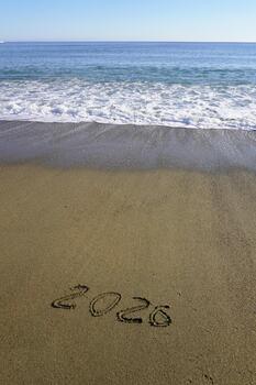 Beach and surf. The inscription 2026 on the sand, a wave at the water's edge, a view of the horizon, a vertical frame. photo