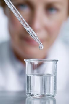 un soltar desde un pipeta terminado un cubilete con un claro solución. en el antecedentes es un borroso hembra investigador, caucásico, de edad mediana. de cerca ver de el laboratorio. foto