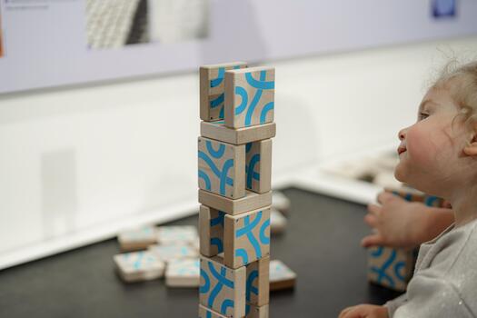 Child plays with wooden building blocks while creating a tall structure at an interactive learning exhibit in a museum photo