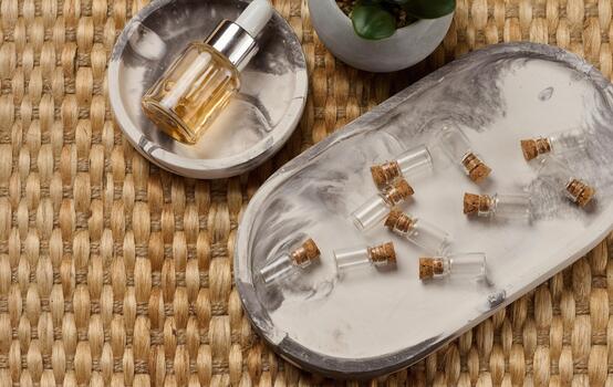 Bottle with a pipette surrounded by small empty bottles with corks. The objects are arranged on a marble tray, a wicker background photo