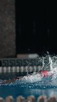 focado nadador dentro vermelho boné poderes através interior piscina faixa, criando dramático salpicos e ondulações dentro baixo luz competitivo Treinamento meio Ambiente video