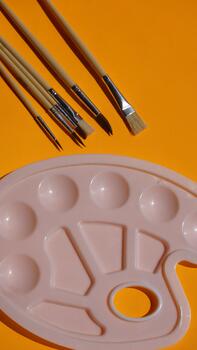 Paint brushes and palette on a yellow background, top view. photo