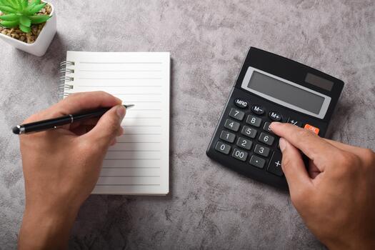 Hands using calculator and writing in notebook on textured desk with plant. photo