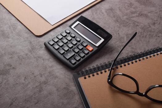 Overhead view of a calculator, eyeglasses, and notepad on a textured desk. photo