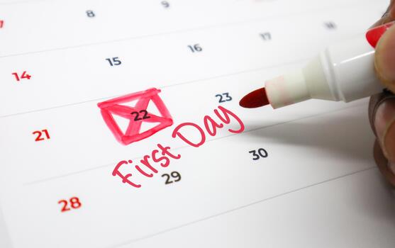 A hand uses a red marker to highlight an important date on a calendar, signifying a First Day or a new beginning and upcoming significant event photo