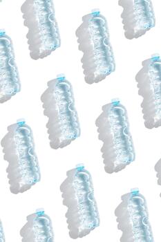 Pattern from Plastic bottles with water at sunlight with sun shadow on white background. Clean drinking water in bottle. Pollution, environment protection concept. World water problem photo