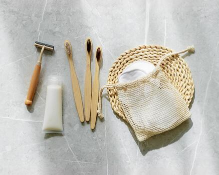 Hygiene products as bamboo toothbrush, toothpaste, reusable pads, safety razor on grey marble background with natural light, eco-friendly items for self care, zero waste concept. Minimal top view photo