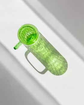 Green colored glass cup with artistic light reflections and caustics on white table. Clear mug for tea and coffee at sunlight with window shadow, summer drink concept, minimal style photo, copyspace photo