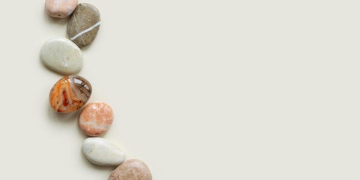 Top view close up colored pebbles sea stones on sand color background. Row from natural round smooth stone neutral tones and sardonyx. Minimal style flat lay, summer concept, empty space photo