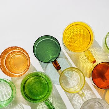 Colored glowing glass cups on white background, casting artistic light reflections and shadows in natural sunlight. Summer drink concept, minimal trend pattern of transparent glasses, caustics photo