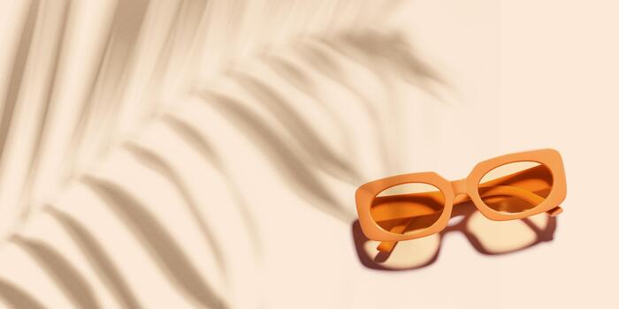 Trendy sunglasses with orange color Frame on beige background at sunlight with palm leaf shadow, beach vibes, summertime mood banner, Summer vacation, rest concept. Minimal layout of eyeglasses photo