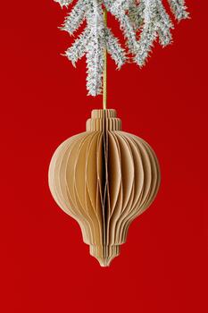 Minimalist Christmas ornament as brown paper flashlight hanging on golden string on snow pine branch on red background. Stylish honeycomb New year festive ball in design, holiday concept, vertical. photo