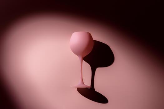 Pink color wine glass in light from spotlight, hard shadow, monochrome. Minimal flat lay dark color. Night party concept. Creative top view wine glass on pink background with shadows around photo