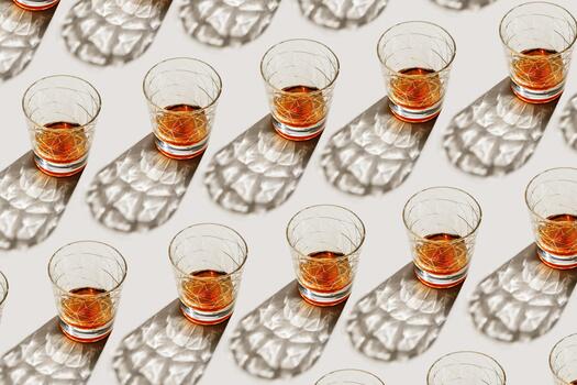 Whiskey Glasses at sunlight, repeated pattern on beige background, minimal neutral layout, aesthetic top view summer still life, refraction at shine alcohol drink, dark shadow, caustics photo