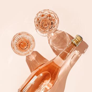 Glasses of rose wine on soft background with shadows from sunlight. Minimal Top view Vintage wineglasses and bottle, sparkling alcohol drink above view with caustics effect from hard light, copyspace photo