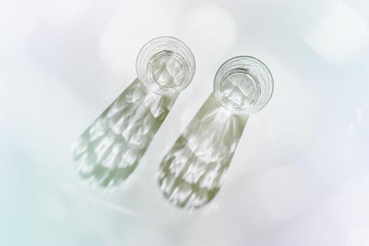 Two Transparent Water Glasses with dark shadows at sunlight on white, pastel color photo minimal style, aesthetic top view shiny cups sparkling at natural light, summer drink, dinamic composition