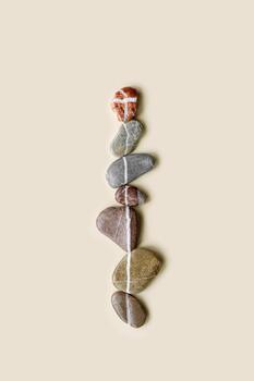 Aesthetic minimal flat lay sea pebble stones with white line, beige background. Composition from natural colored stone on the same level. Balance or harmony concept, vertical row rocks. photo