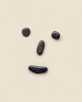 Anthropomorphic face from black colored sea stones on beige background, cheerful, happy, joyful mood, smile on the face. Summer creative flat lay, minimal style, top view photo
