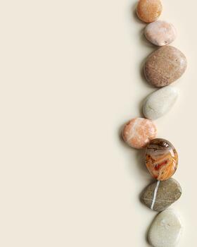 Aesthetic minimal flat lay with sea pebble stones on beige background with copy space. Row from natural smooth stone pastel color and sardonyx gemstone. Summer concept, top view photo
