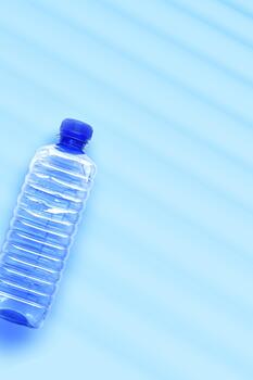 Blue-tinted plastic water bottle close up on light blue background with light reflections and shadow, copyspace. Minimal aesthetic top view photo, one transparent blue bottle, overview vertical image photo