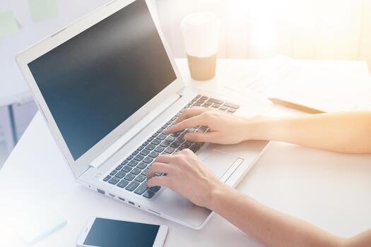 Close up of old woman's hands on keyboard of lap top, people working at home, using pc and smartphone concept, modern white notebook with blank screen on table. Internrt, work, technology concept. photo