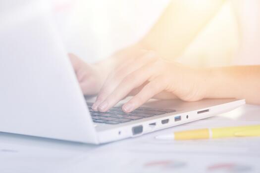 Woman's hands typing on keyboard of notebook, sitting at table against white background, white lap top and yellow pen on desk, female working online via Internet, checking her e mail, has message. photo