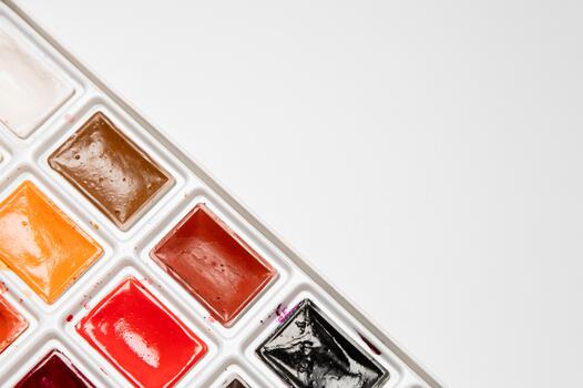 close-up of a box of watercolors in small compartments on a white background. Viewed from above, with a white background for text and advertising. Creative backdrop photo