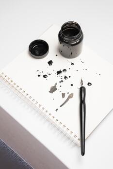 Calligraphy training. A close-up top view of a pen and ink bottle, creative attempts, and the resulting smudges and ink stains on the paper in a notebook photo
