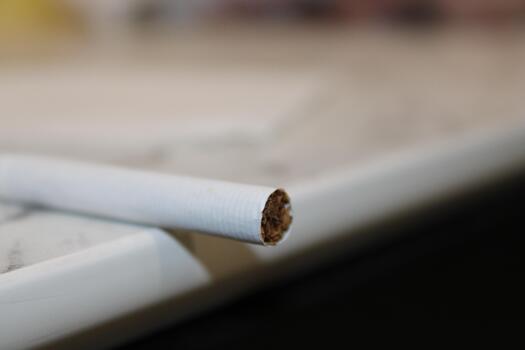 Cigarette resting on a table with blurred background and surface details in a indoor setting photo