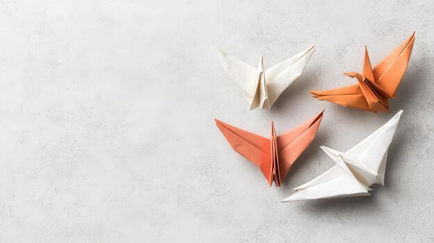 Four paper cranes in soft orange and white sit on a textured light grey surface, symbolizing imaginative thought and graceful movement. photo