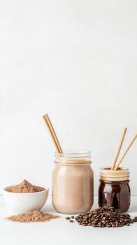 Cocoa powder and coffee beans next to jars with beverages and straws on white surface. photo