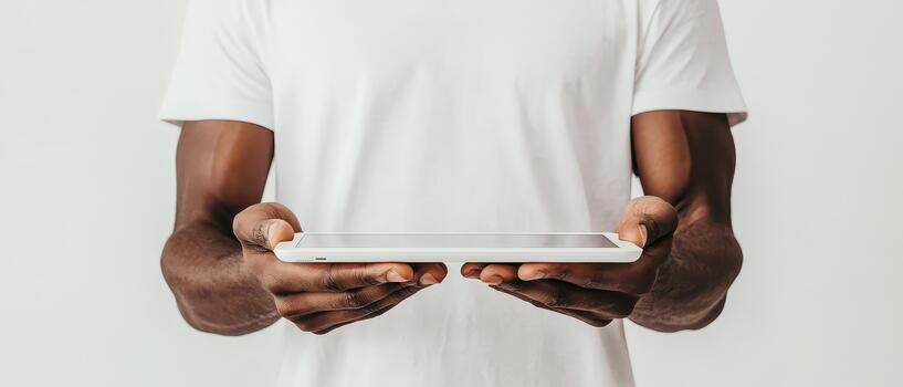Man wearing white shirt holding a modern tablet device with both hands against a plain light background. photo