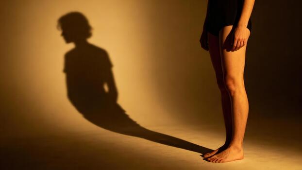 Standing female figure casting an elongated, ominous shadow on a warm, golden-lit backdrop, emphasizing internal conflict and identity. photo