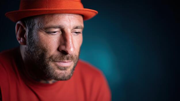 Man in red hat looking down with contemplative expression against dark background portrait close up studio shot with copy space photo