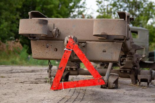 Rear view of a dirty, parked vehicle with a red warning triangle positioned behind it on a dirt surface. photo