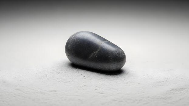 A smooth dark gray stone is positioned on a white slightly textured surface under soft diffused lighting. photo