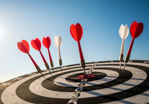 A dartboard under clear blue skies features multiple darts with red and white flights. photo