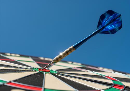 A dartboard is shown with a blue dart hitting the bullseye against a clear blue sky. photo