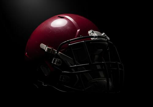 Dark monochromatic image of a football helmet, prominently showcasing a maroon color with contrasting black background photo