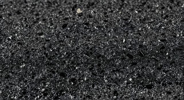 Close-up macro shot of a textured black surface with tiny reflective particles, showcasing a dark, gritty abstract background photo