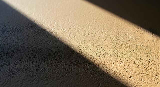 Abstract play of light and shadow across a rough, sand-colored textured wall, creating a dynamic visual contrast and highlighting the intricate surface details photo