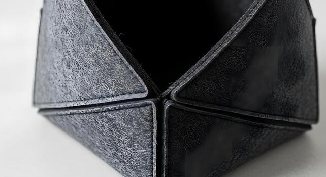 Close-up detail of a dark, distressed geometric object showcasing intricate texture and craftsmanship, with visible stitching and faceted surfaces creating an abstract, modern design photo