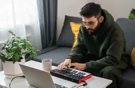 Man recording electronic music track with portable midi keyboard on laptop computer in studio. Producing and mixing music beat making and arranging audio content with professional audio devices photo